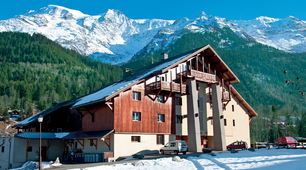 A classic 1970s alpine building with large apex roof and dark wood balconies on each floor